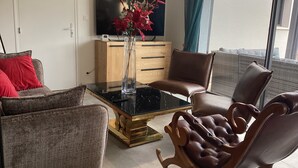 A modern living room with a glass coffee table, leather armchairs, a wooden cabinet, and a flat-screen TV. - A 5-minute walk from Port Bail Beach: house with an enclosed garden. (Port-Bail-sur-Mer)