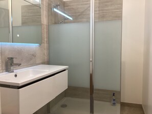 Ein modernes Badezimmer mit einer in Glas eingefassten Dusche, einem weißen Waschbecken und einem Spiegel.