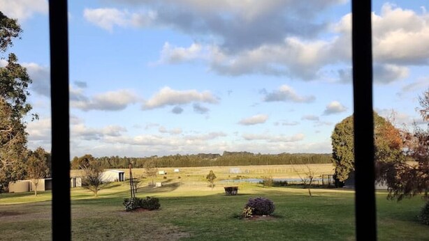 A view through a window of a grassy field with trees and a clear sky. - Hunter Valley Nulkaba | breathtaking views & relax (Nulkaba)
