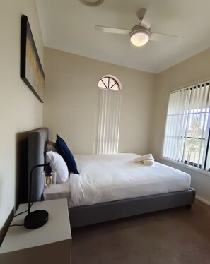 A bedroom with a bed, a ceiling fan, a nightstand, and a window with blinds. - Hunter Valley Nulkaba | breathtaking views & relax (Nulkaba)