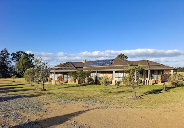 A two-story house with a solar panel on the roof, surrounded by a grassy area and trees. - Hunter Valley Nulkaba | breathtaking views & relax (Nulkaba)