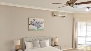 A bedroom with a bed, nightstands, a ceiling fan, an air conditioning unit, a window with blinds, and a painting on the wall. - Hunter Valley Nulkaba | breathtaking views & relax (Nulkaba)