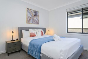 A neatly made bed with a blue blanket, a gray headboard, and a bedside table with a lamp. - The Pond sweet 4 br home by Coles with&WiFi (The Ponds)