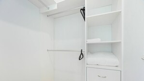 Een witte kast met hangstang, een plank met opgevouwen kleding en een ladeblok.