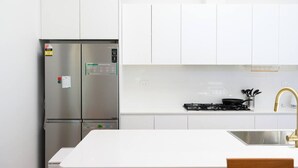 Een moderne keuken met witte kasten, een roestvrijstalen koelkast, een gasfornuis en een spoelbak met een gouden kraan.