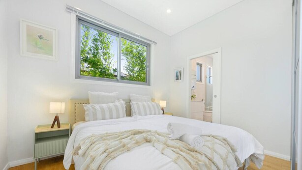 Een slaapkamer met een groot bed, twee nachtkastjes, een raam met uitzicht op groen en een deur naar een andere kamer.