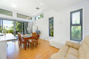 A modern living space with a dining area, a sofa, and large windows. - Large Family-Friendly House｜Central Riverwood Stay (Riverwood)