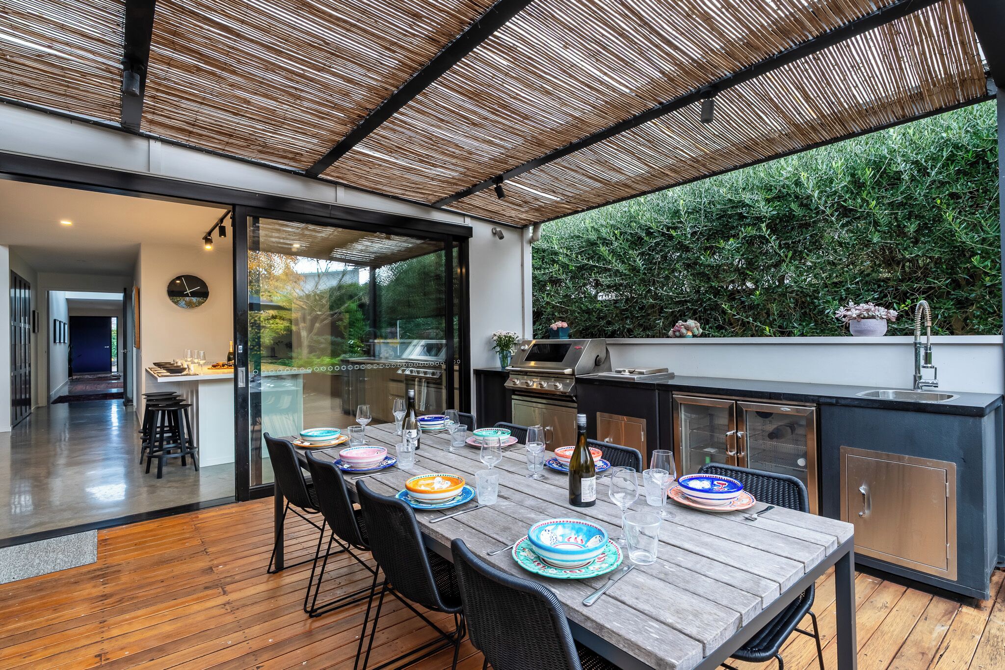 An outdoor dining area with a wooden table set for four, a grill, and a sink.
