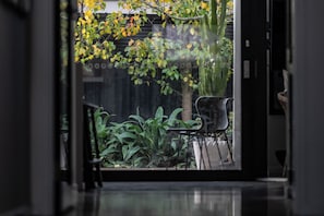 Blick durch eine Glastür in einen Raum mit einem Sessel, einem Tisch und einer Pflanze.