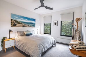 Een slaapkamer met een bed, een plafondventilator, een nachtkastje met een lamp, een raam met jaloezieën en een hoedrek aan de muur.