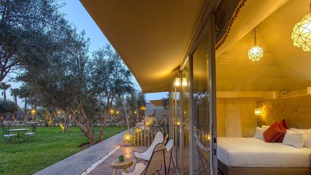A hotel room with a bed, a seating area with chairs, and a view of the garden.