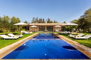 A swimming pool with lounge chairs and umbrellas, surrounded by trees and a building.