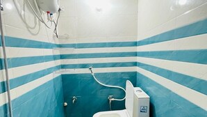 A bathroom with a toilet, a shower, and a blue bucket on a small stool. - Roomshala Shreeji Palace  (Ayodhya)