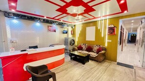 A hotel reception area with a red and white counter, a sofa, a coffee table, and a ceiling fan. - Roomshala Shreeji Palace  (Ayodhya)