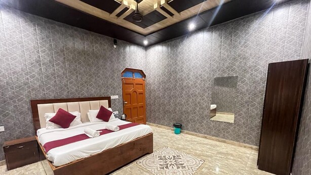 A bedroom with a bed, a wooden wardrobe, a small trash bin, and a patterned rug. - Roomshala Shreeji Palace  (Ayodhya)