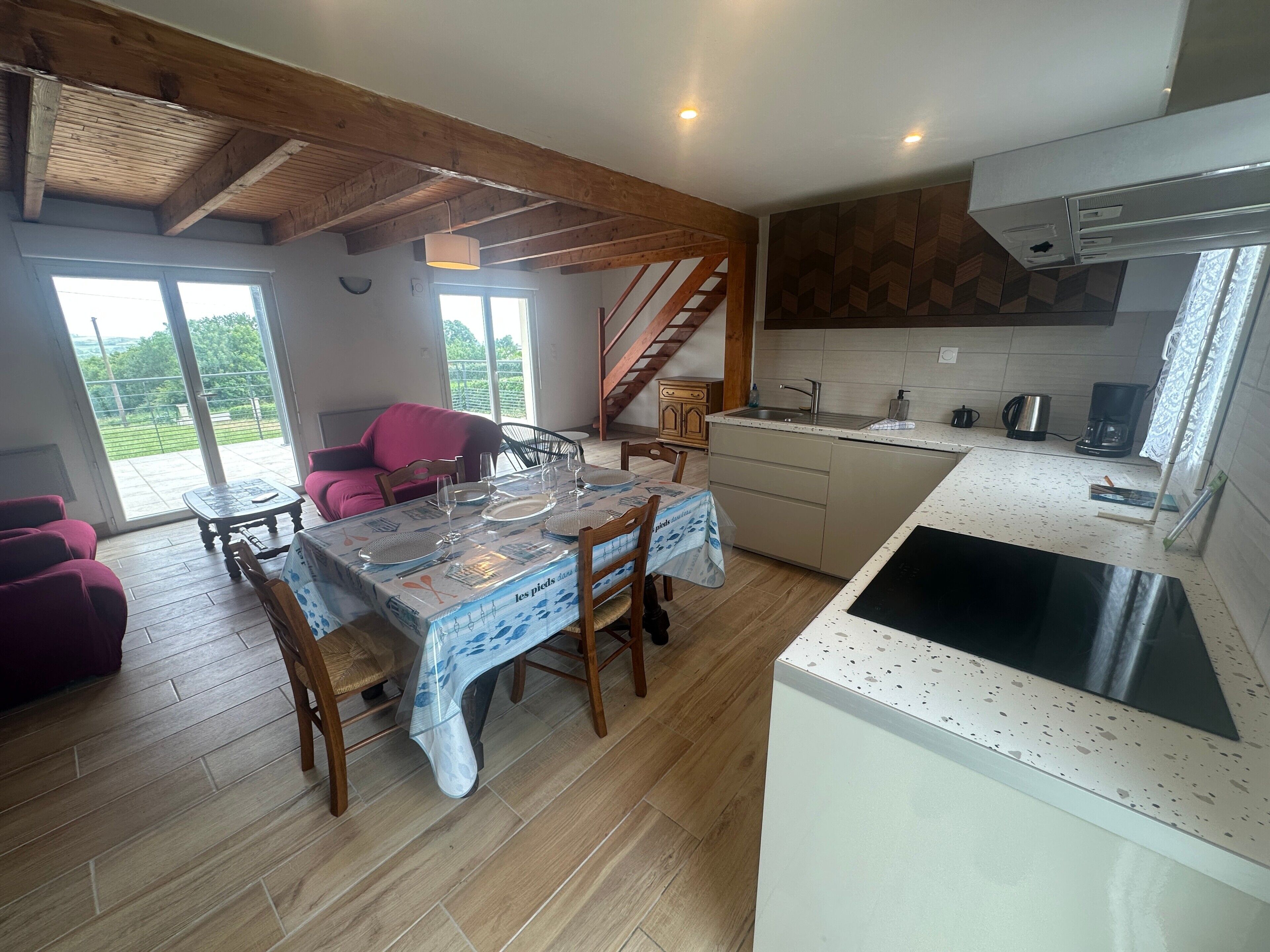 A dining area with a table set for four, a kitchen with a stove and sink, and a staircase leading to an upper level.