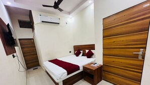 Ein Hotelzimmer mit Bett, Holzschrank, Deckenventilator, Klimaanlage und einem kleinen Nachttisch mit einer Zeitschrift.
