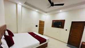 Ein Hotelzimmer mit einem Bett, einem Deckenventilator, einem an der Wand montierten Fernseher und einer Tür.