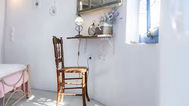 A room with a bed, a chair, a small table with a lamp, a mirror, and a window with curtains. - TWIN OVEN APARTMENT (messaria)