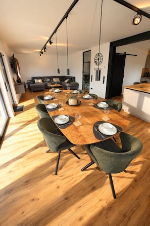 A modern dining area with a wooden table set for six, surrounded by green upholstered chairs.