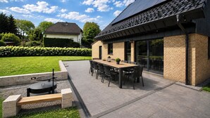 An outdoor patio area with a dining table and chairs, a barbecue grill, and a brick wall. - Vennchalet - Vacation Home for 8 People with a Sauna and Hot Tub (Monschau)