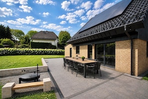 Eine Außenpatio-Terrasse mit Esstisch, Stühlen, Grill und Ziegelfassade.