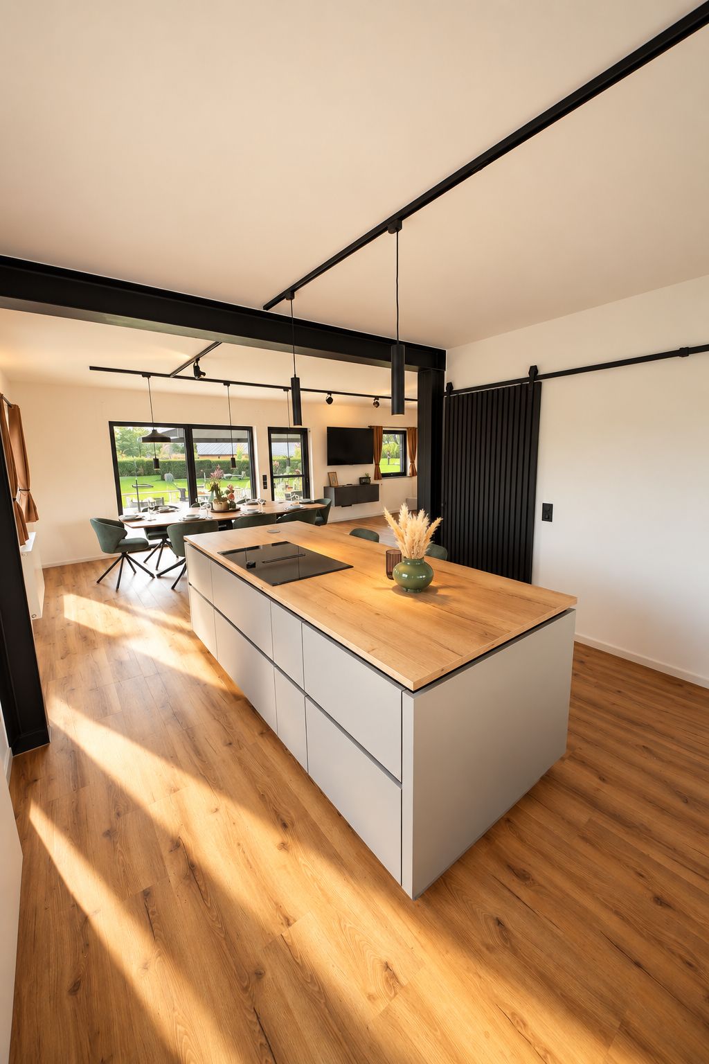 Eine moderne Küche mit einer großen Kochinsel, Holzboden und Blick ins Freie.