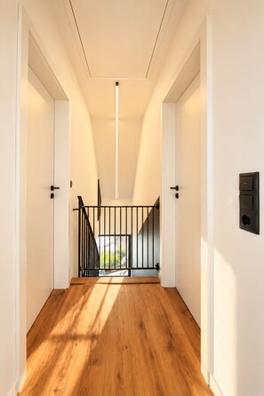 A spacious hallway with wooden flooring, a black metal railing, and a light fixture on the ceiling.