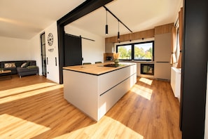 A modern kitchen with a central island, wooden flooring, and large windows providing natural light.