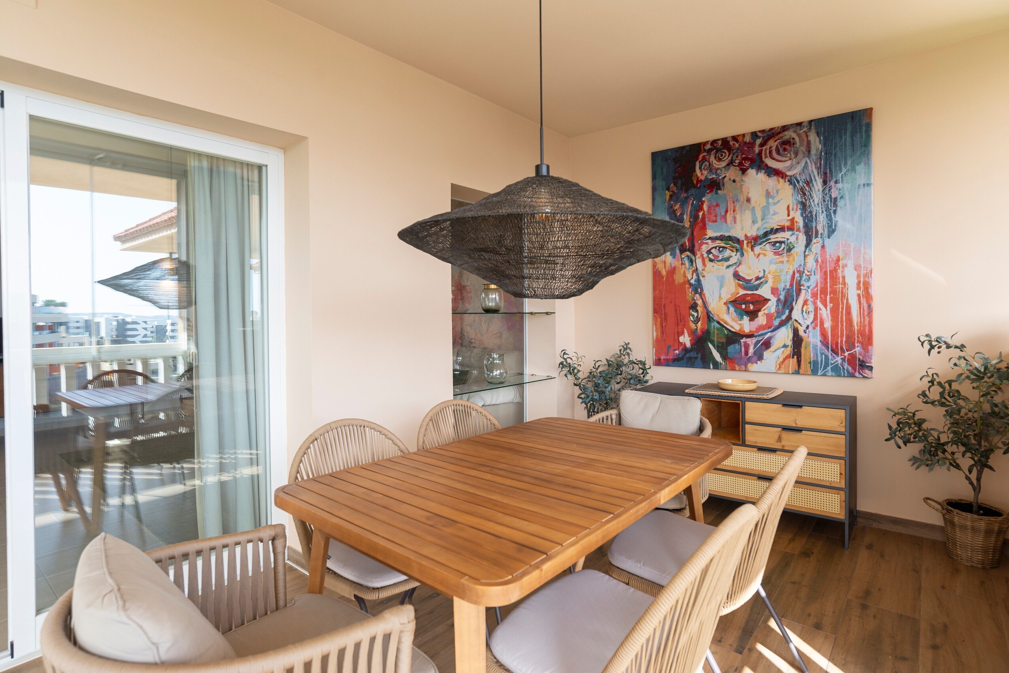 Een eetgedeelte met een houten tafel, rieten stoelen en een hanglamp.