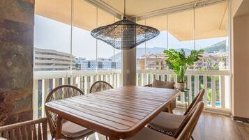 En balkon med et træbord og stole, en hængende lampe og udsigt til bygninger og bakker.