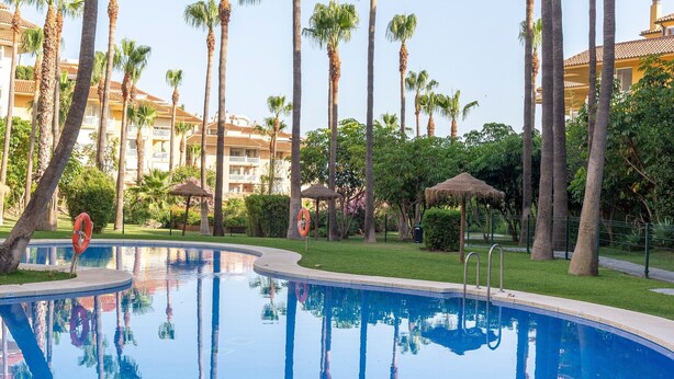 A swimming pool surrounded by tall palm trees and a building with balconies in the background. - Holiday Home 'Cozy 3BR Apartment Higuerón' with Mountain View, Wi-Fi and Air Conditioning (Benalmádena)