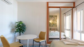 A hotel room with a bed, a small table, two chairs, a potted plant, and a large mirror reflecting the room. - Holiday Home 'Cozy 3BR Apartment Higuerón' with Mountain View, Wi-Fi and Air Conditioning (Benalmádena)
