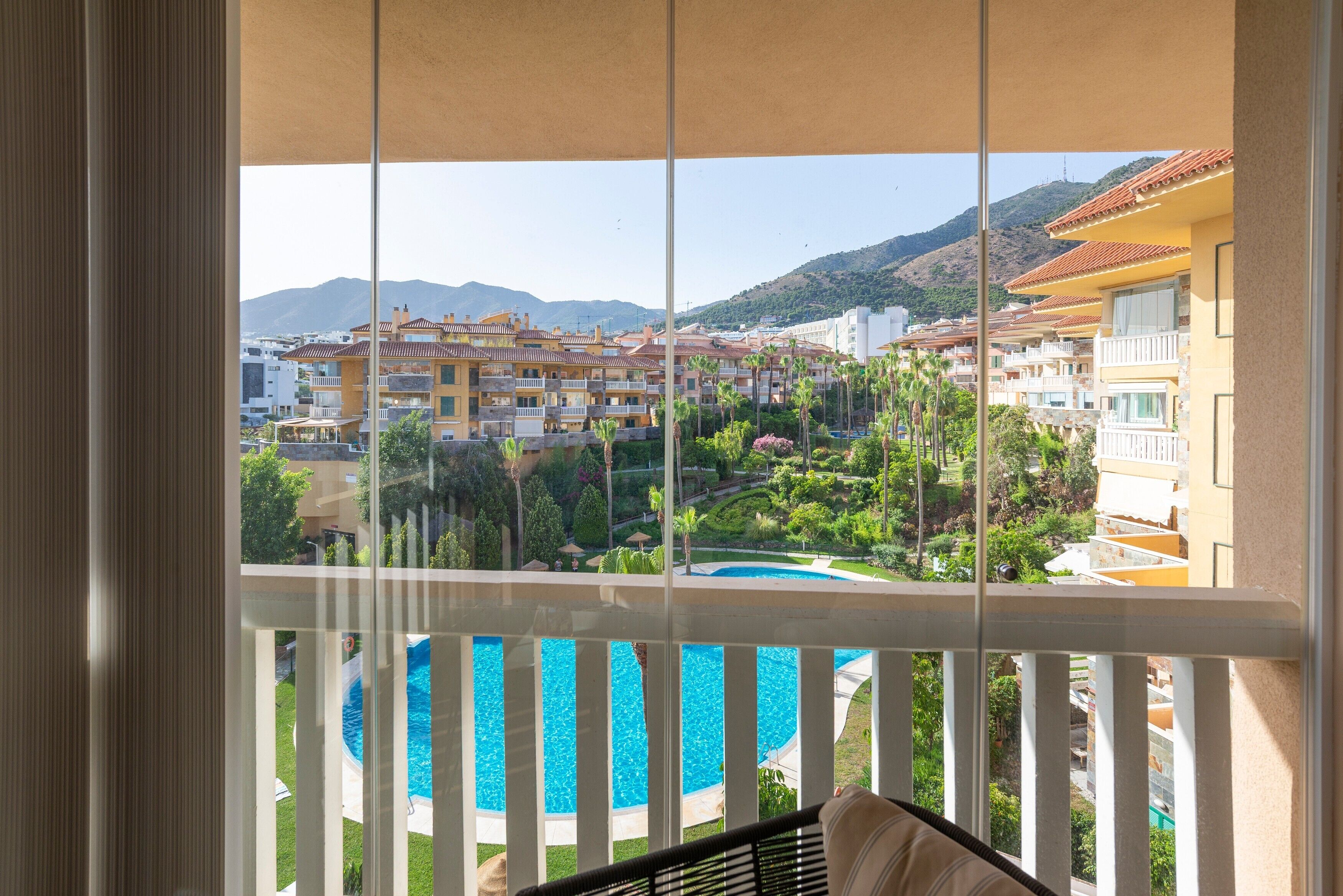 A balcony with a view of a swimming pool, a mountain, and hotel buildings.