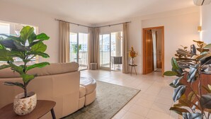 A modern living room with a sofa, a potted plant, and a view of the outdoors through large windows. - Holiday Home 'Cozy 3BR Apartment Higuerón' with Mountain View, Wi-Fi and Air Conditioning (Benalmádena)