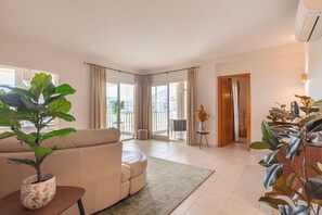 Una sala moderna con sofá, planta en maceta y vista al exterior a través de amplios ventanales.