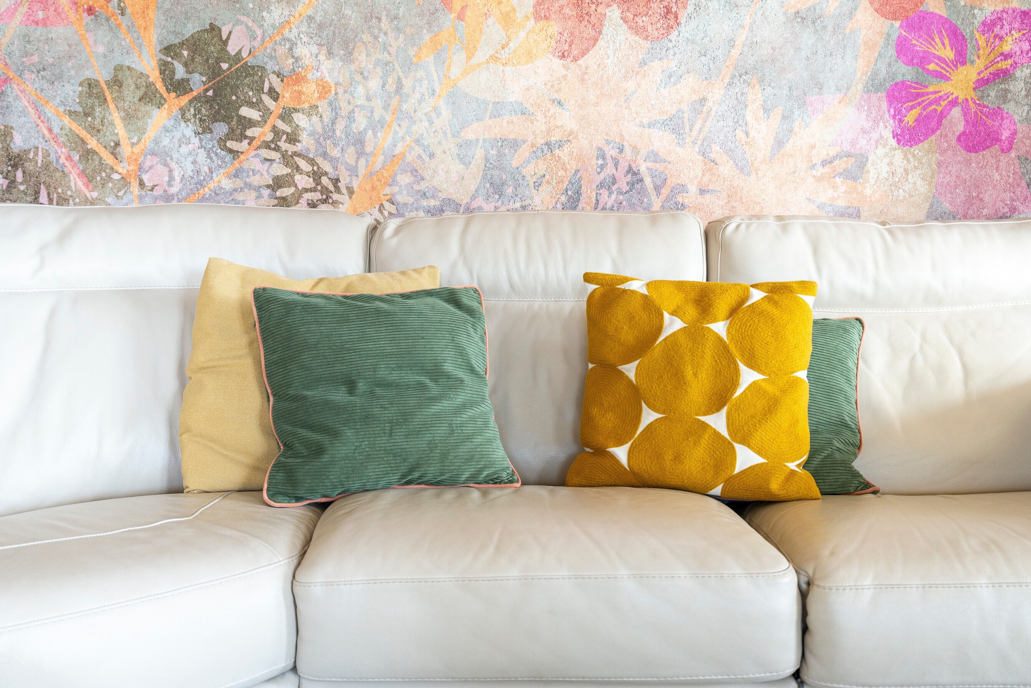 Un canapé en cuir blanc avec trois coussins de couleurs et de motifs différents.