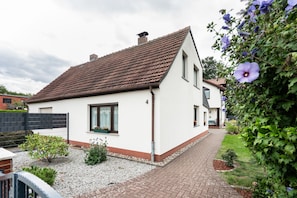 A two-story house with a tiled roof, a paved driveway, and a garden with flowering plants.