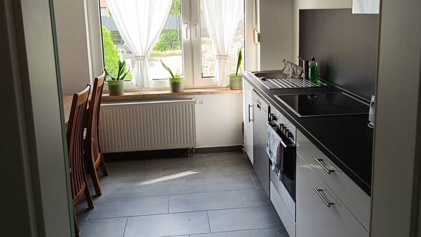 Una cocina con radiador, estufa, lavabo y ventana con cortinas.