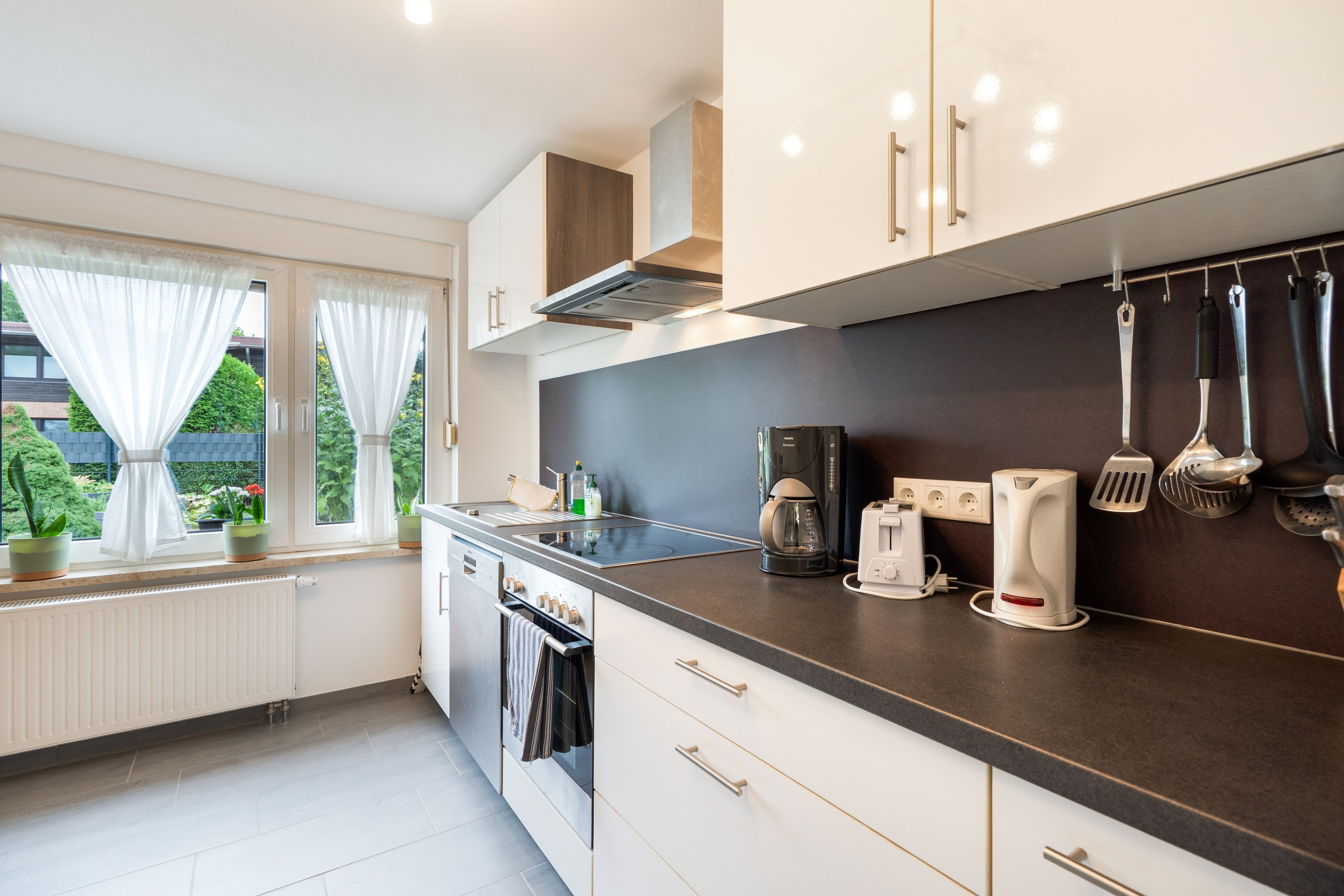 Une cuisine moderne avec un plan de travail noir, des meubles blancs et une fenêtre agrémentée de rideaux.