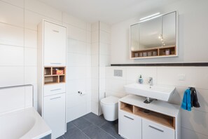 A modern bathroom with a white sink, mirror, and storage cabinets.