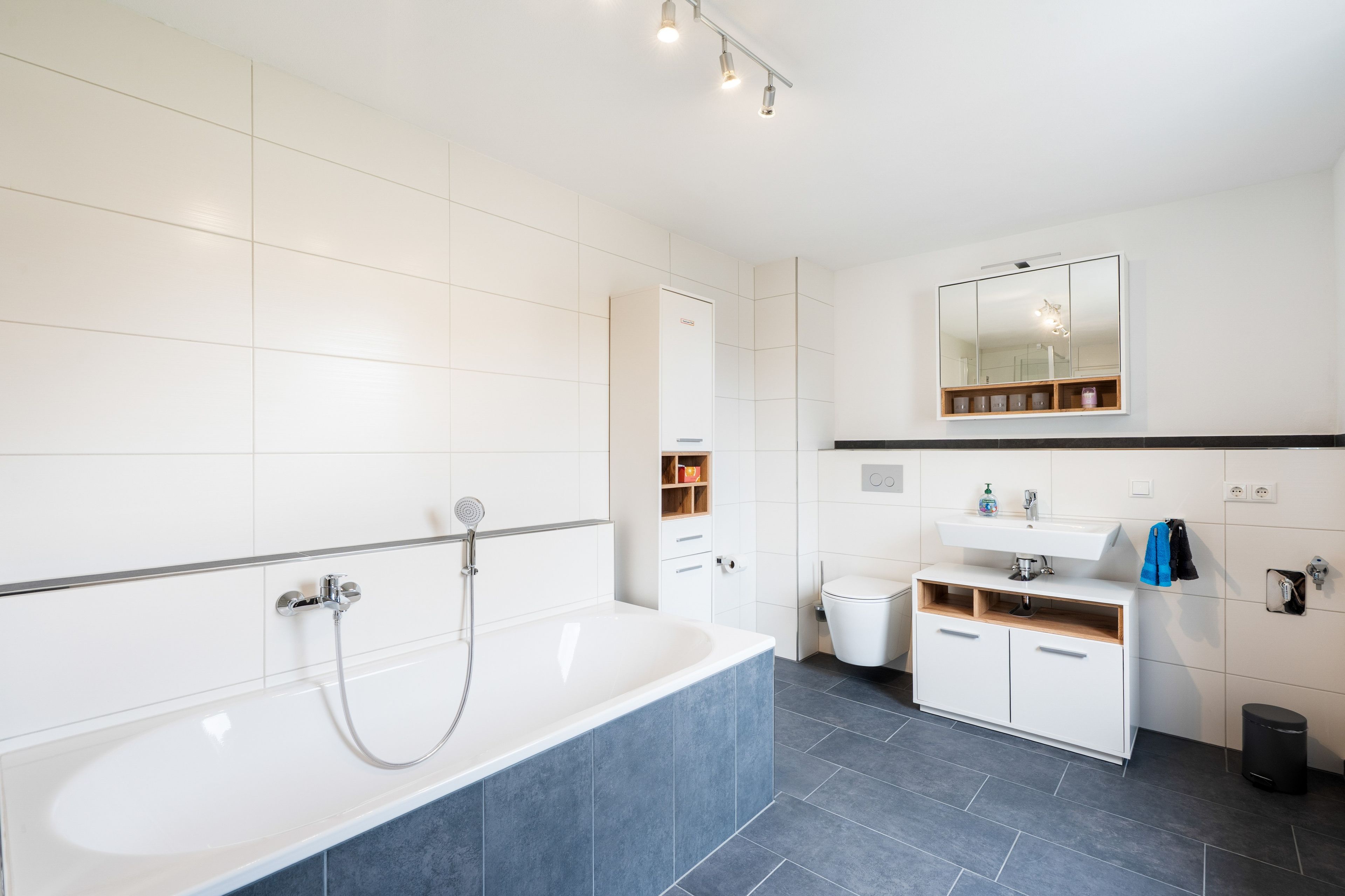 A modern bathroom with a white bathtub, a toilet, and a sink with a mirror above.