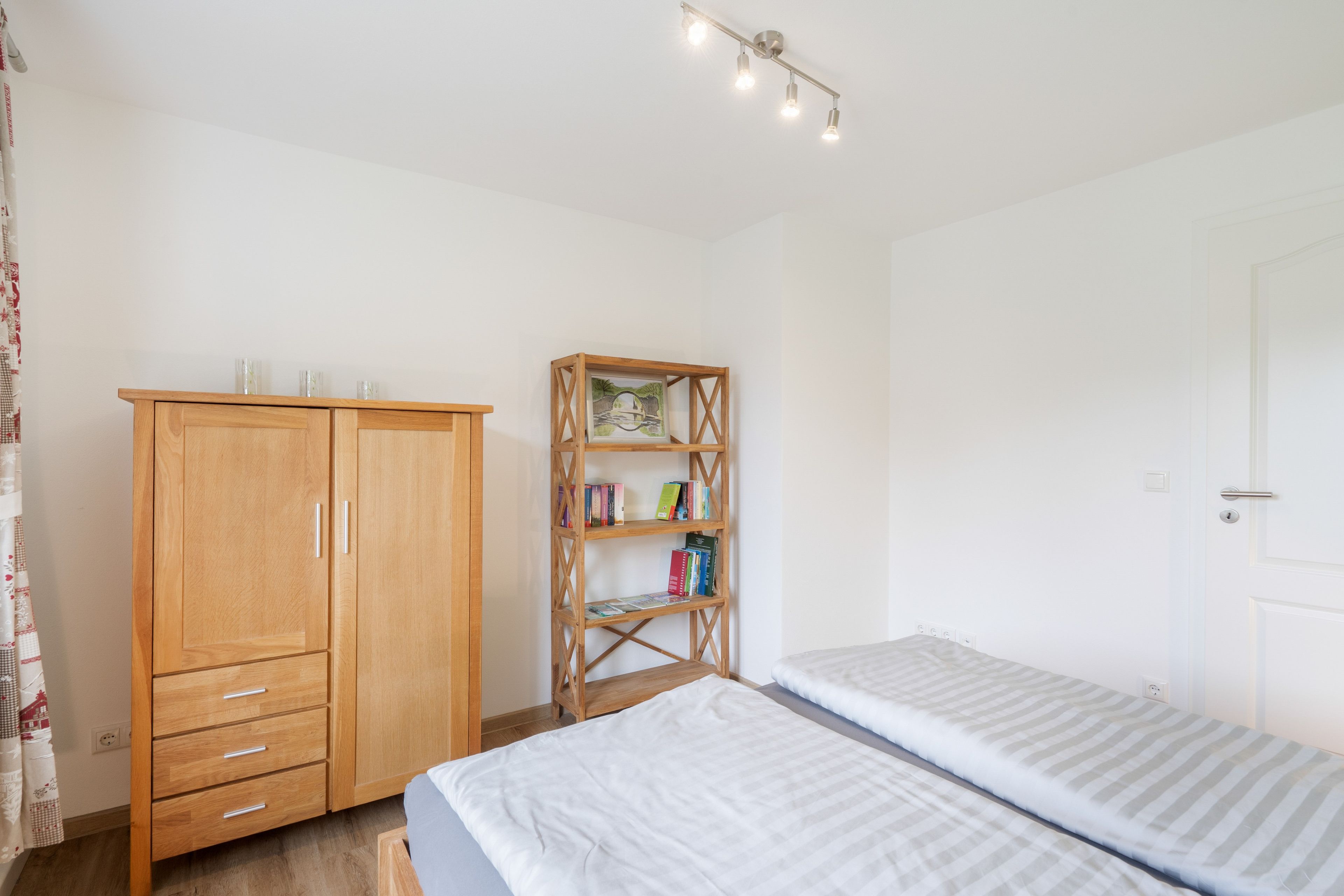 Une chambre avec une armoire en bois, une bibliothèque en bois et un lit recouvert d’une couverture à rayures.