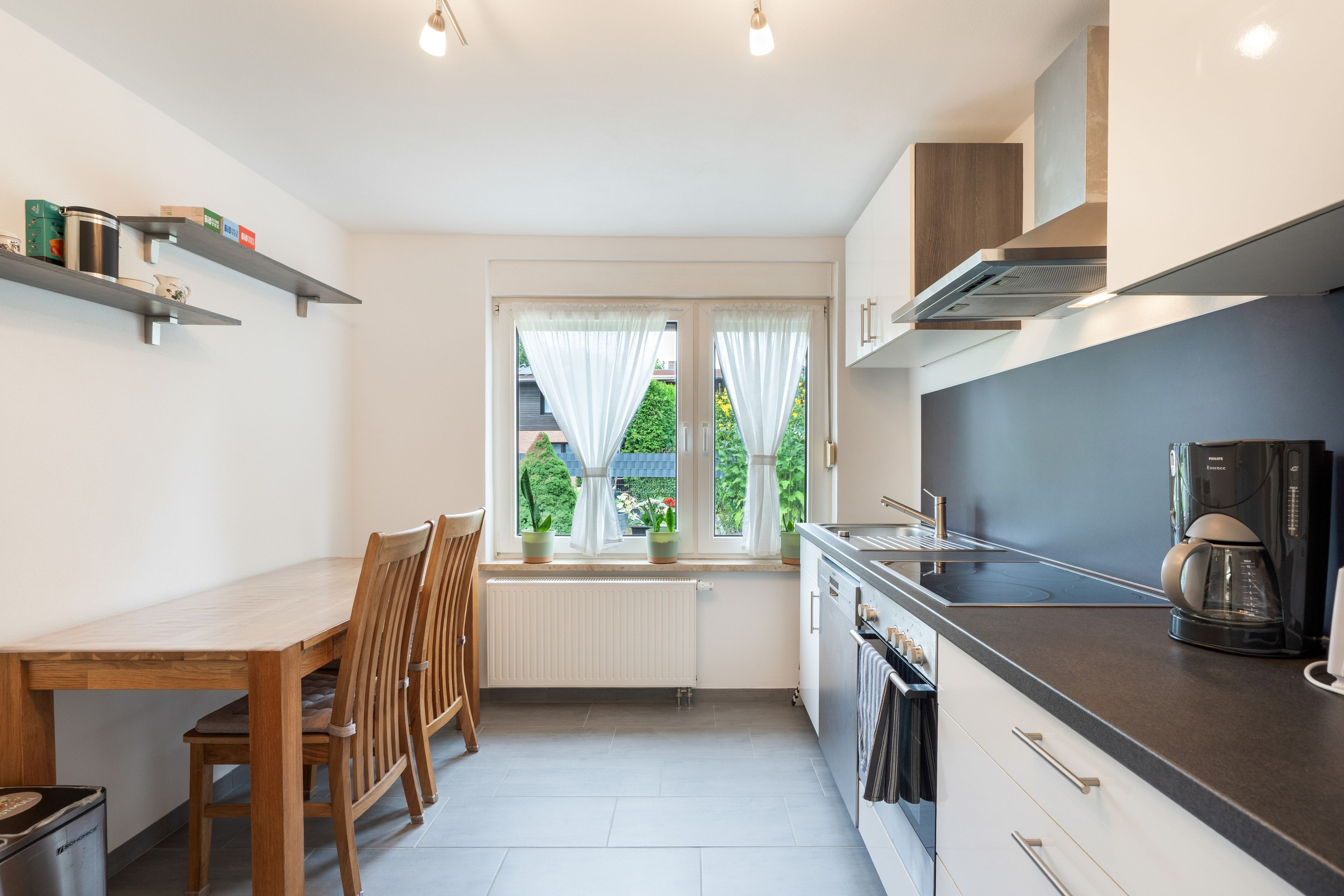 A compact kitchen with a dining table, chairs, a coffee maker, and a window with curtains.