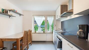 A compact kitchen with a dining table, chairs, a coffee maker, and a window with curtains.