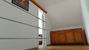 Una habitación con techo inclinado, un armario de madera, barandilla de vidrio y un cuadro en la pared.