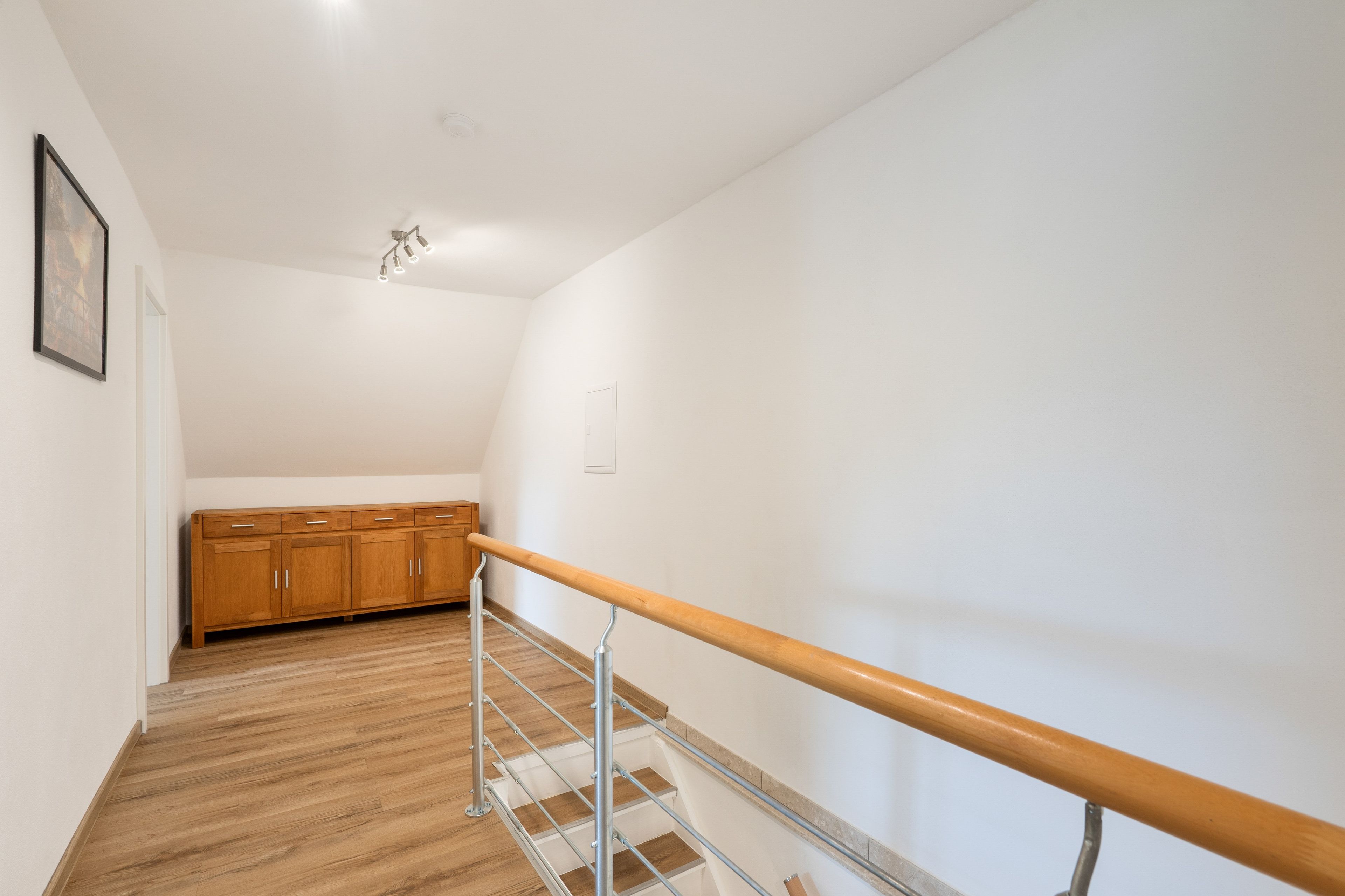 Un escalier avec une main courante en bois et des balustrades en métal, menant à un espace où se trouvent des meubles en bois.