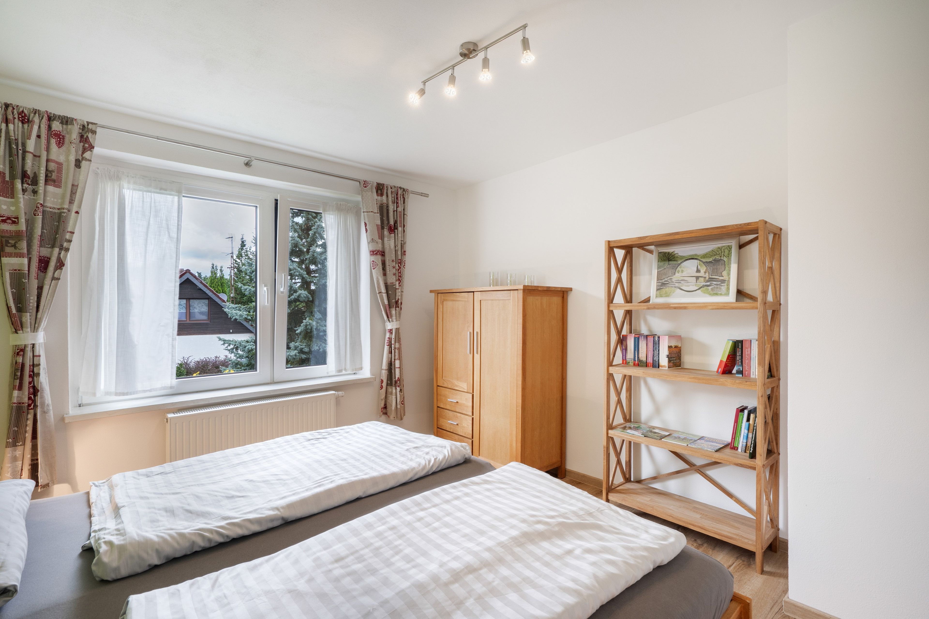 A bedroom with two beds, a wardrobe, a bookshelf, and a window with curtains.