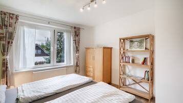 A bedroom with two beds, a wardrobe, a bookshelf, and a window with curtains.