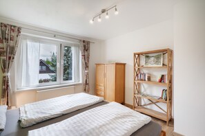 Un dormitorio con dos camas, un armario, una estantería y una ventana con cortinas.